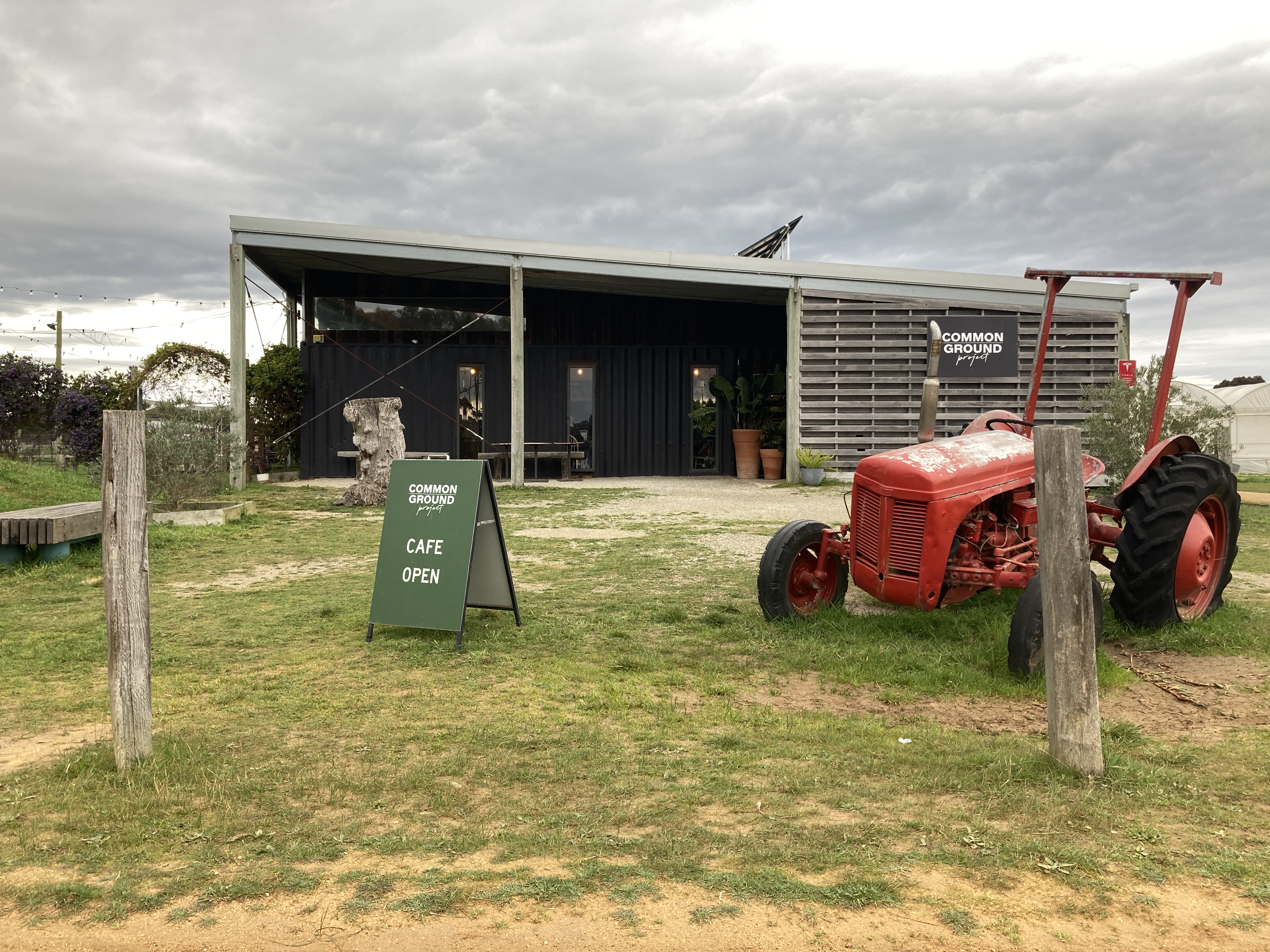 Image of the front entrance to the Common Ground Project. We see the entrance to the cafe, an open sign and old red tractor out the front. 