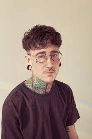 Julz Evans masculine presenting person short dark hair glasses tattoo on neck