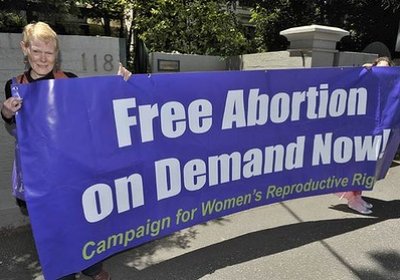 Debbie Brenan with banner Free abortion on demand white writing on purple background