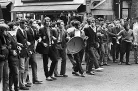 Black and white image of the Paris Riots 1968: young people lined up with steel bin lids and linked arm in arm