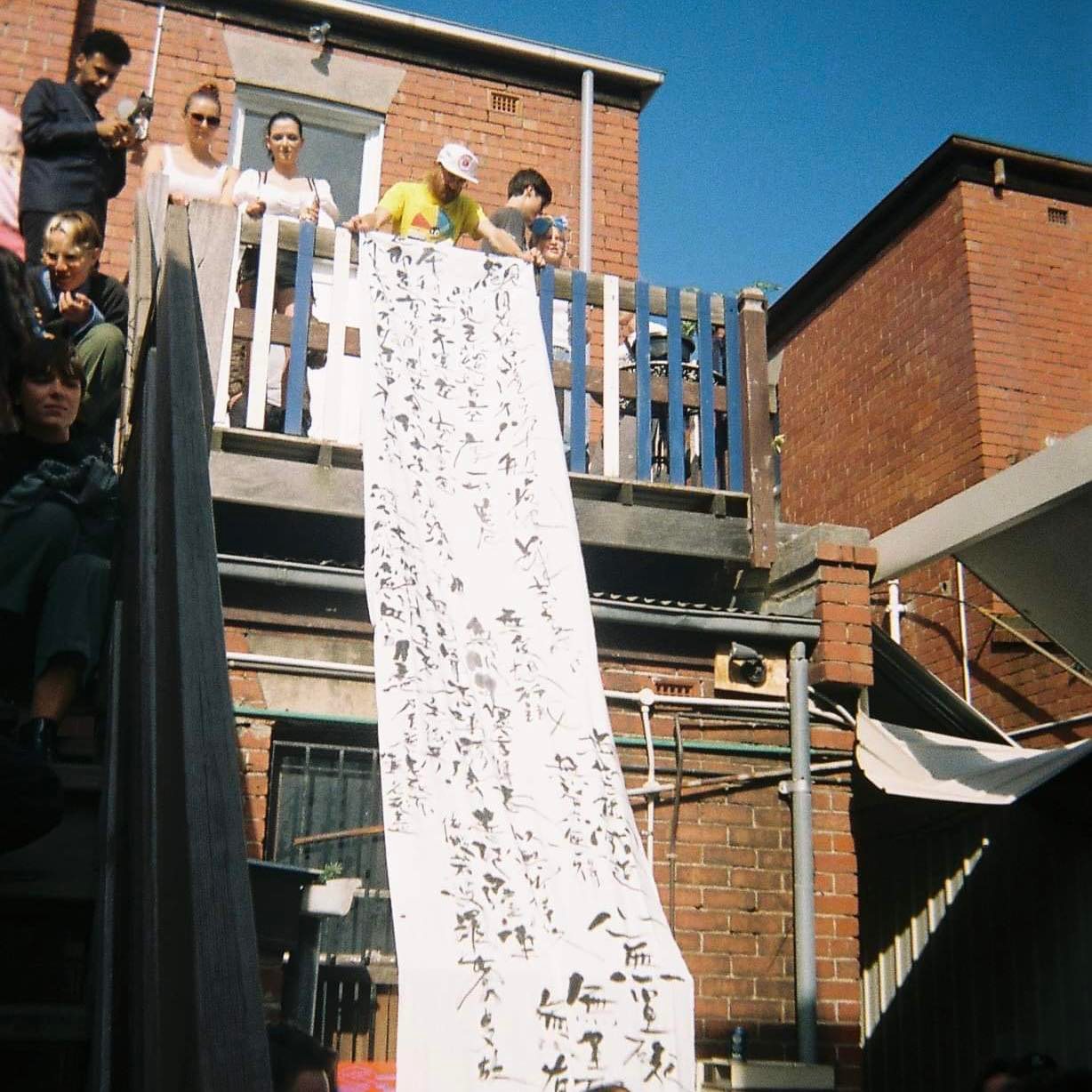 The heart sutra written in black calligraphy on a long white banner at the Narrm launch of HER 他 in 2020, shortly before the first COVID lockdown.