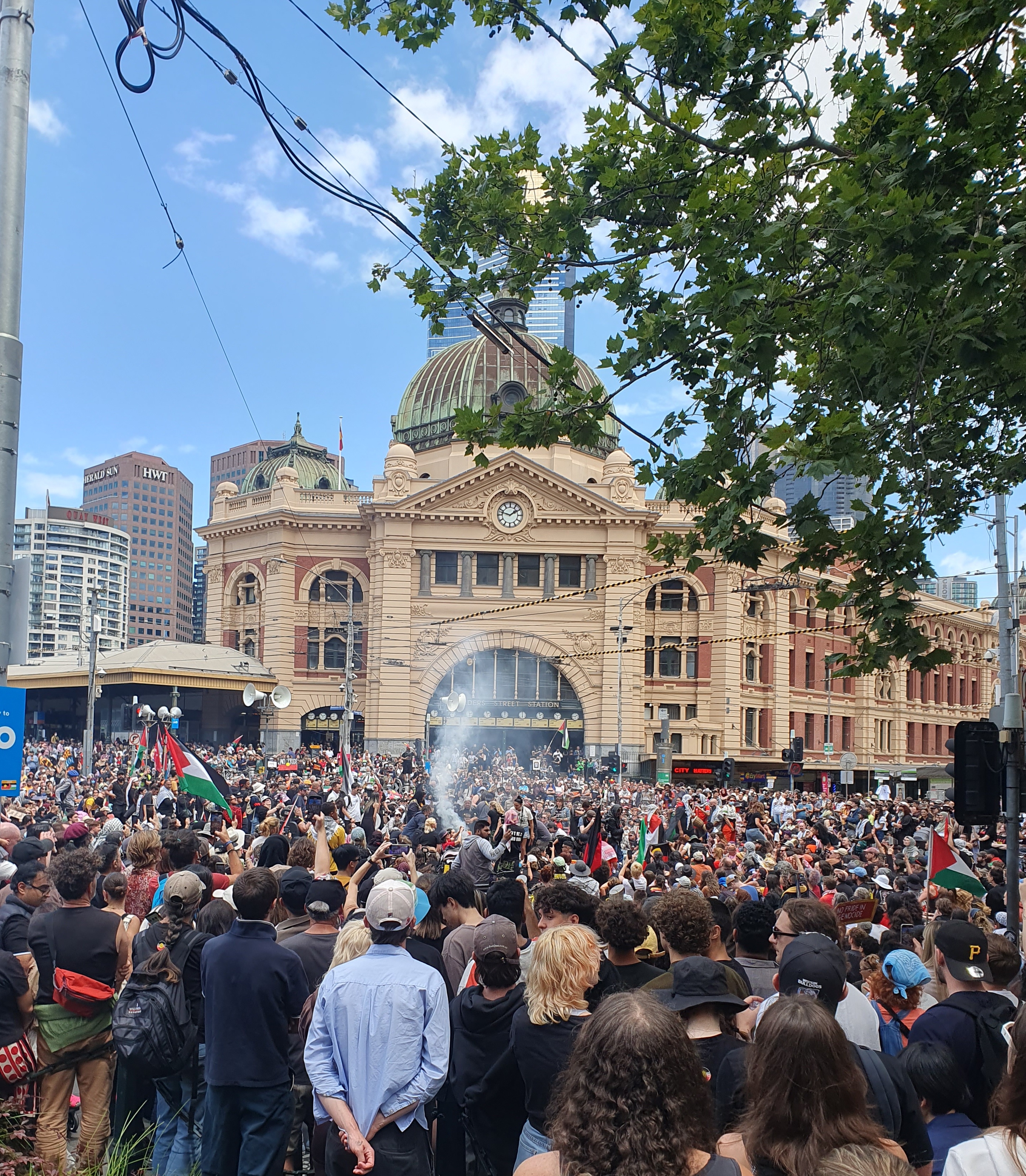 Smoke rises from near dancers at the centre of the crowd in front of Flinders Street station on Invasion Day 2024