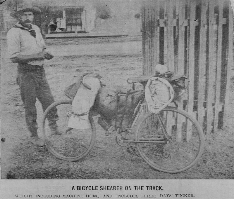 A C19th shearer stand next to his bicycle which is covered in bags and swags. 