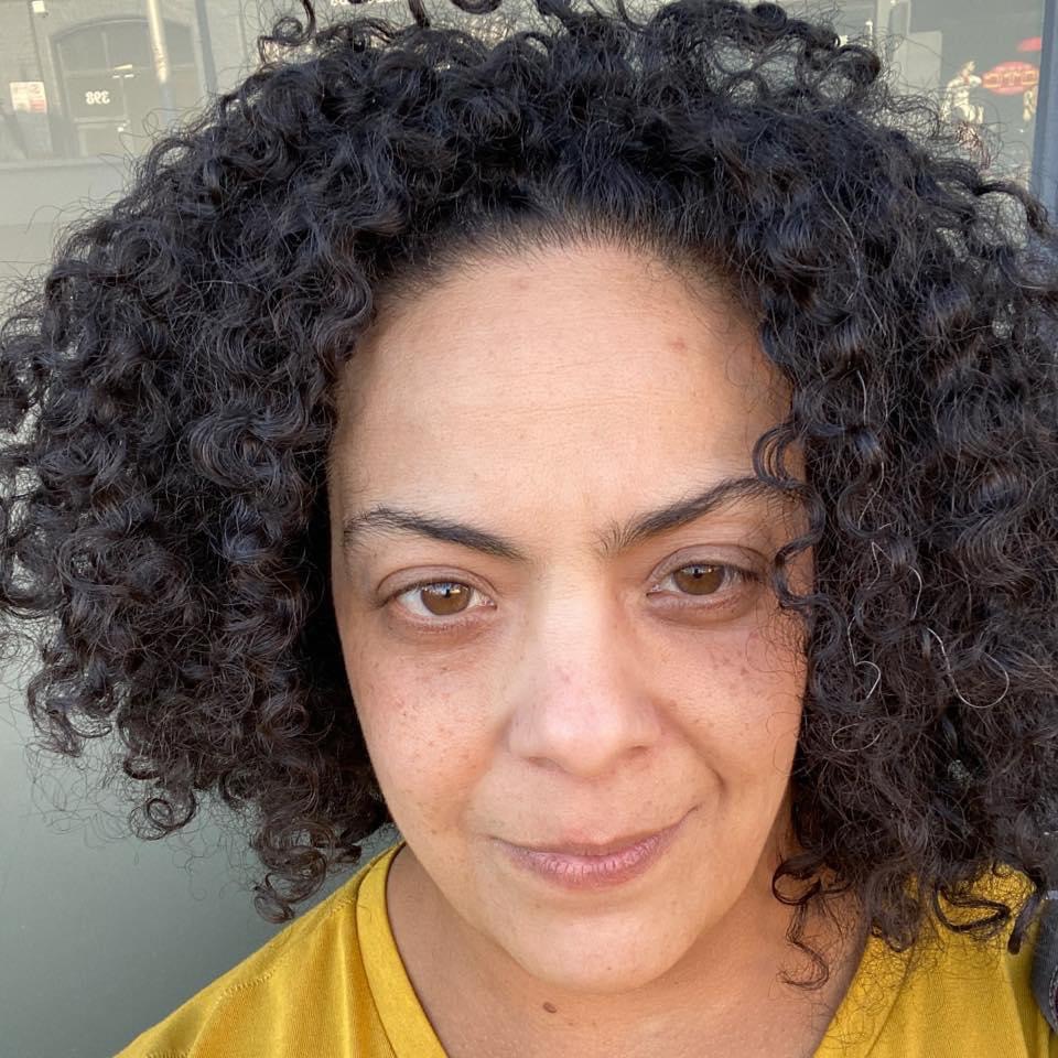 A woman with black curly hair looks into the camera with a faint smile