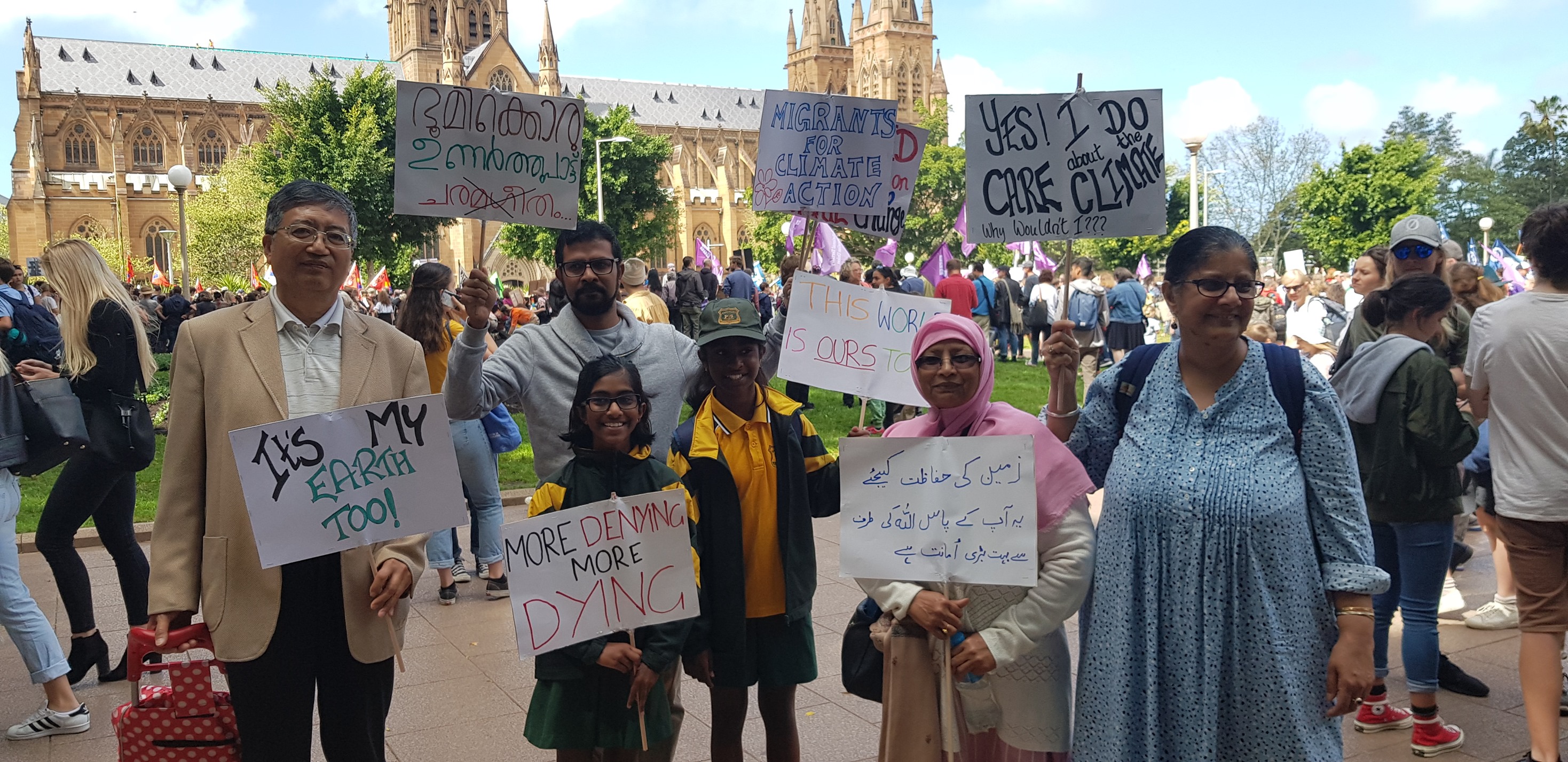 A group of racially diverse migrants hold signs in English and Arabic at a protest for climate justice.