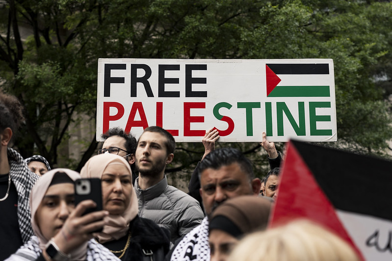  photograph of Free Palestine protesters at a Melbourne rally. They wear keffiyahs and centred in the photo is a sign reading "FREE PALESTINE". 