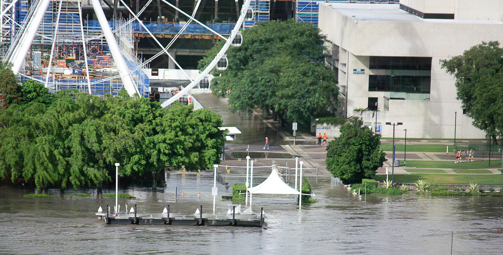 Photo of Brisbane's Southbank during the 2011 floods. Floods engulfing green trees, white ferris wheel, blue construction and grey buildings.