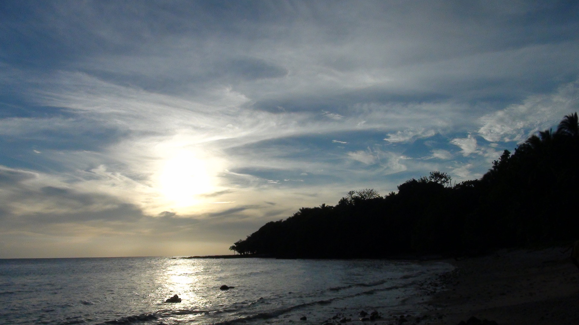 Vanuatu beach with sun emerging from clouds and vegetation. 