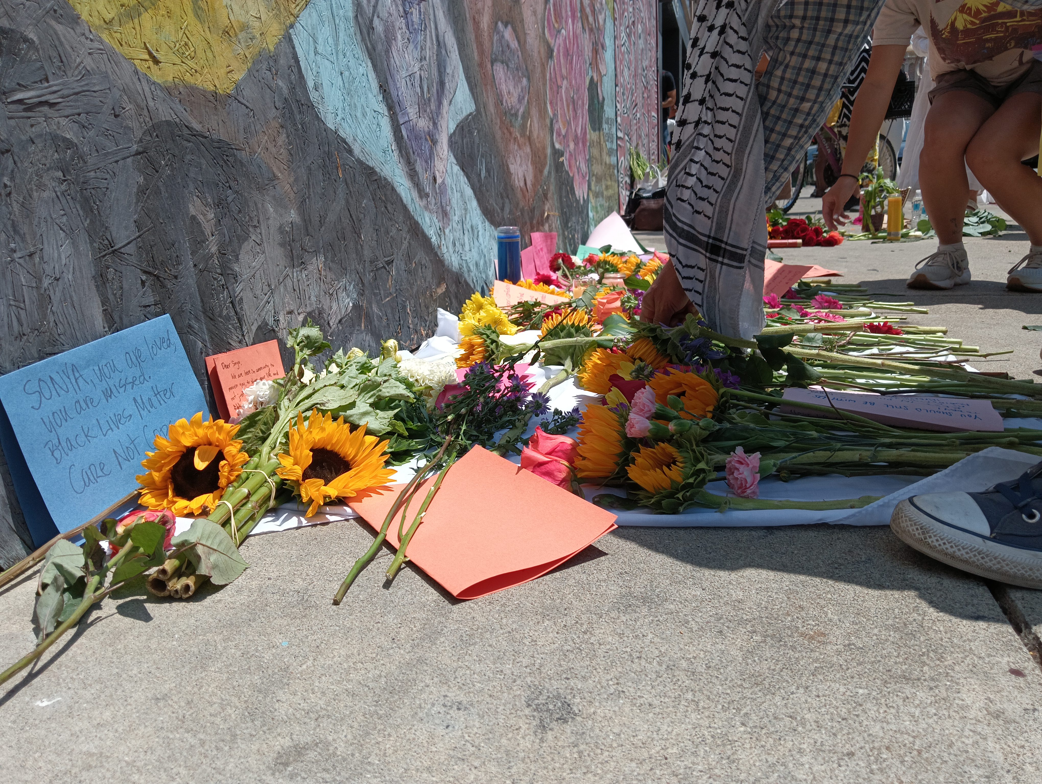 People laying flowers and handwritten notes at a street-side altar set up to honour Sonya Massey.