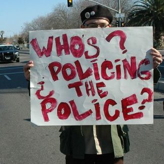 a person holding up a sign stating whos policing the police 