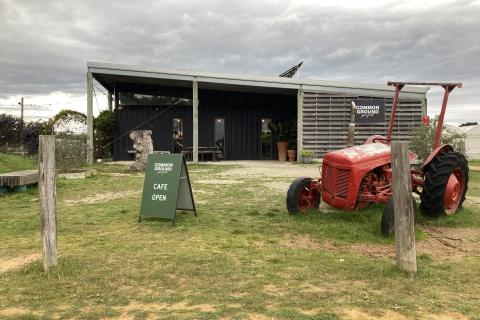 Image of the front entrance to the Common Ground Project. We see the entrance to the cafe, an open sign and old red tractor out the front. 