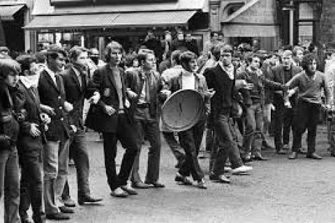 Black and white image of the Paris Riots 1968: young people lined up with steel bin lids and linked arm in arm