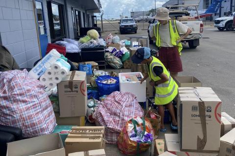 Two people wearing yellow fluro vests work with boxes and bags of supplies on the tarmac at Cairns airport