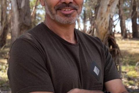 A man standing with his arms crossed and smiling with eucalypts in the background 