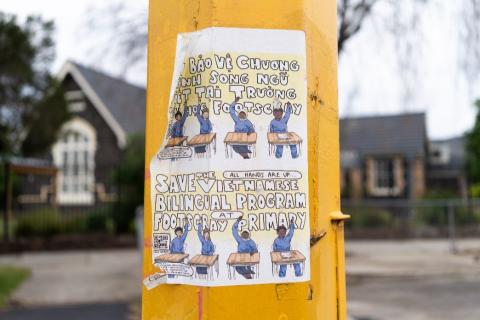 Paper campaign poster with an illustration of children at school desks reading "Save the Vietnamese bilingual program at Footscray Primary", ​in both English and Vietnamese, stuck on a yellow post with one corner peeling free.