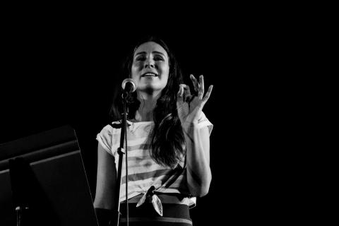 A young woman standing behind a microphone, performing spoken word poetry