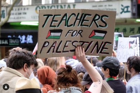 A person holding up a cupboard placard in a crowd that reads Teachers for Palestine