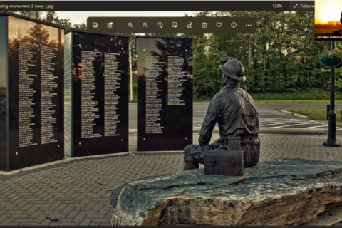 Screenshot from webinar with image of a memorial to miners with three large black square columns at back with names in white on them, and bronze sculpture of miner sitting in foreground. In the top right corner is a small image of Lorraine Rekmans, a middle aged First Nations woman with glasses, pale complexion and pinkish hair.