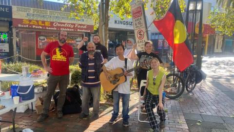 Image shows the community kitchen crew set up to serve some delicious meals with musical instruments and Aboriginal flags.