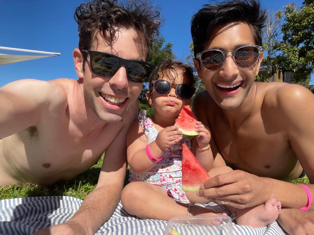 Adrian, Jasmine, and Govind are at the beach. They are smiling at the camera.