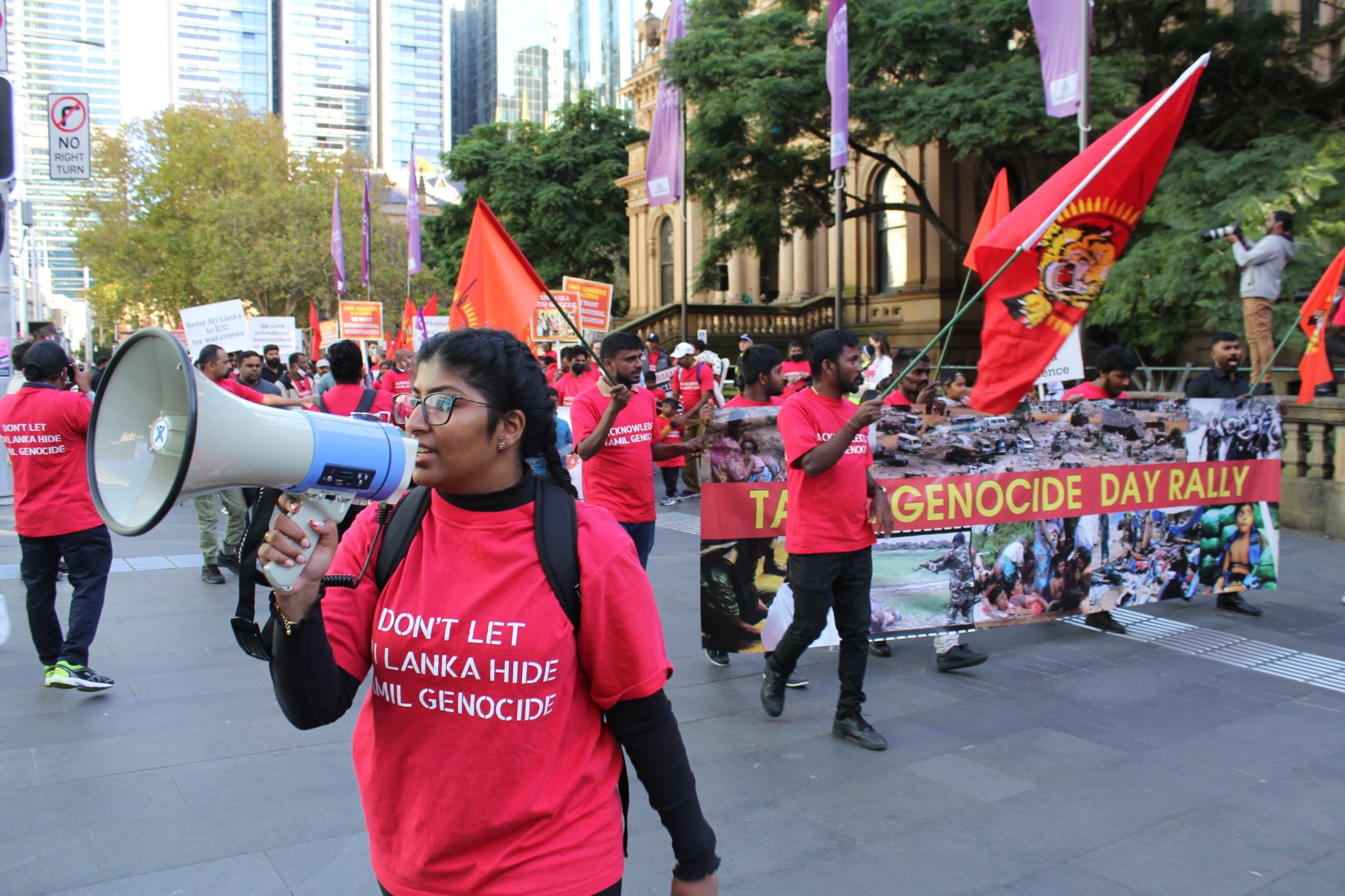 Tamil Refugee Council protestor hold microphone in front of marching protesters holding banners