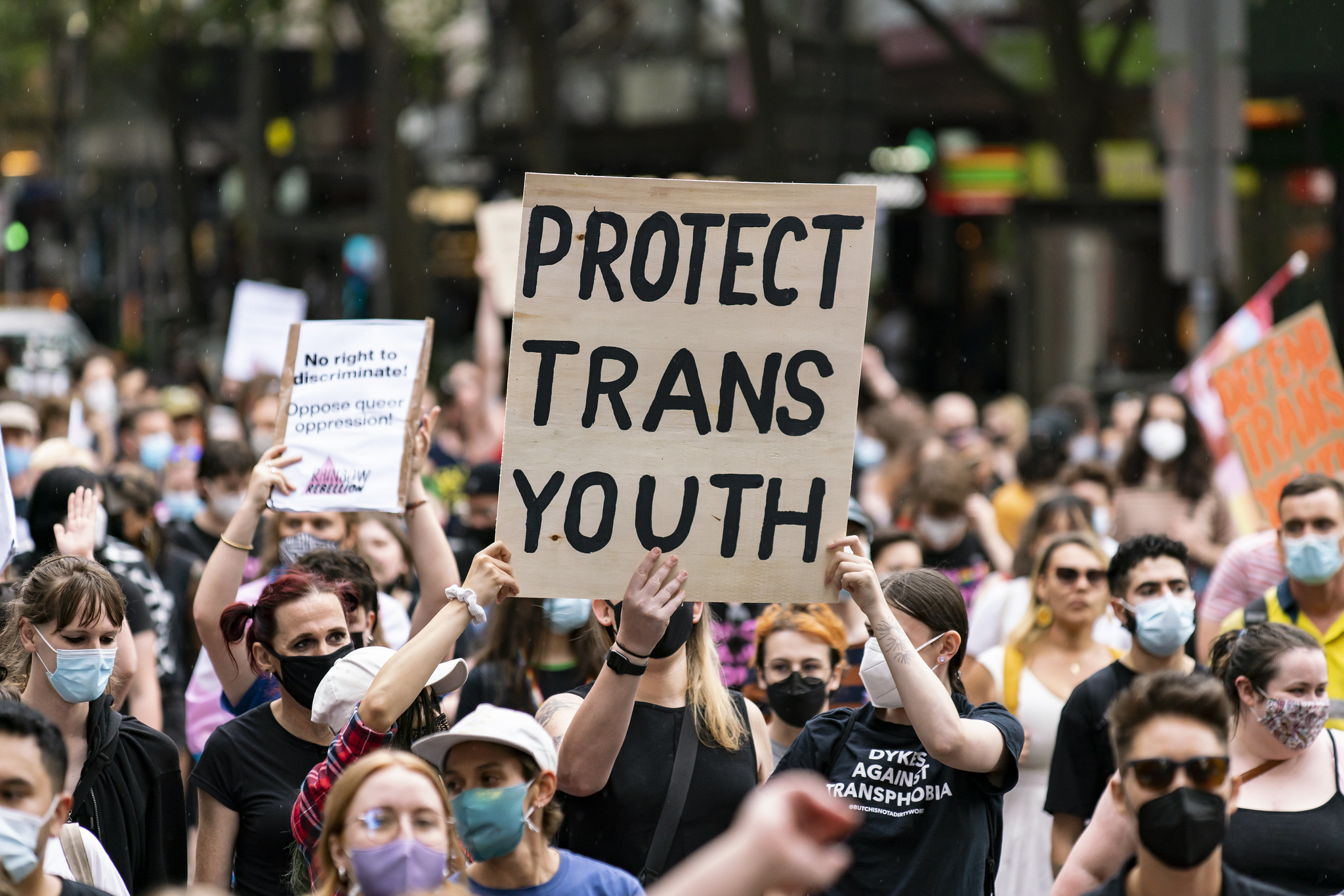 A crowd of protestors for trans rights, with one prominent cardboard sign in the foreground that reads "Protect Trans Youth".