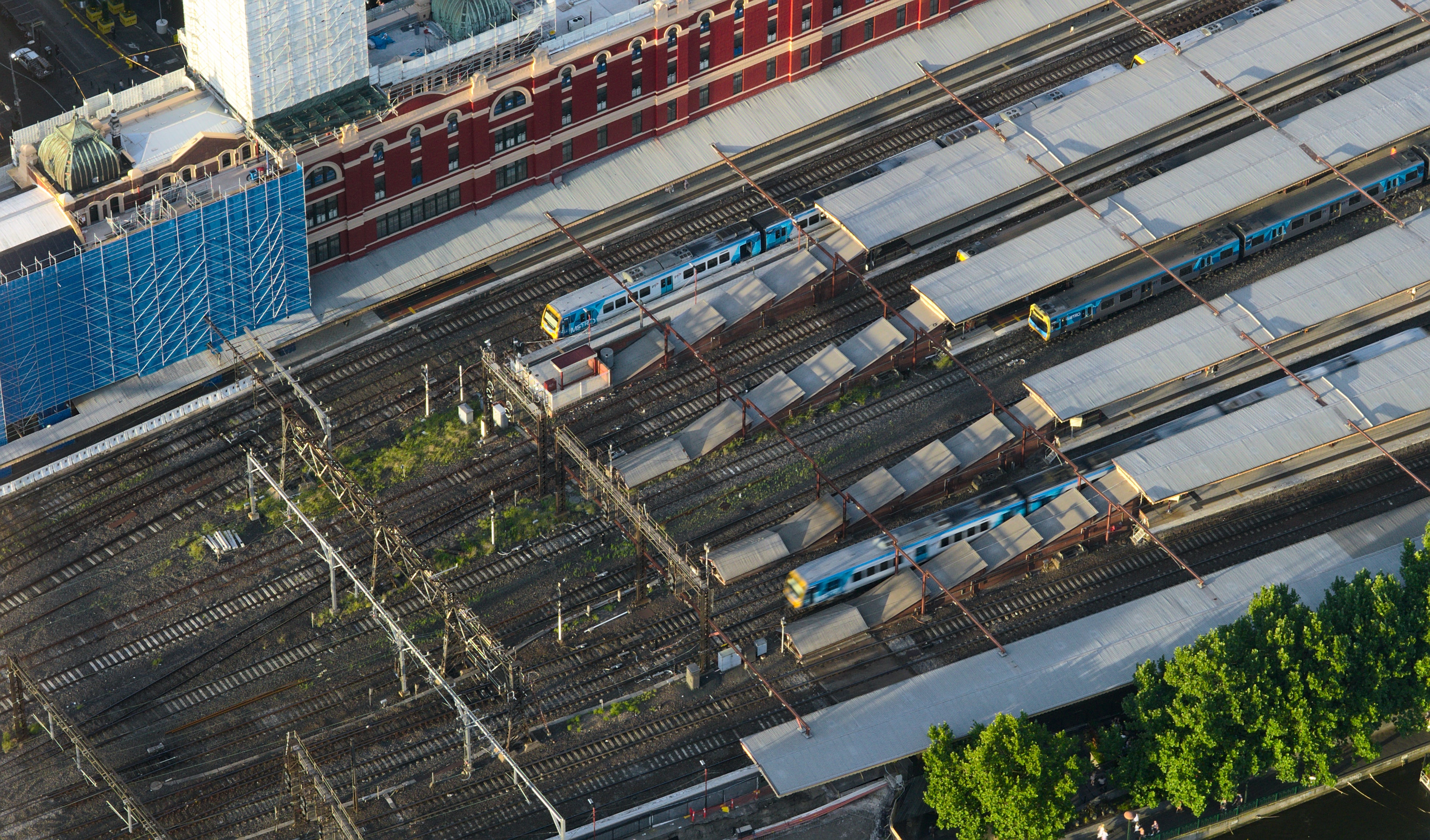 Aerial photo of approximately twelve platform roofs and railway tracks, Flinders Street Railway station in Melbourne, Australia. There are some metropolitan passenger trains both stationary and moving through some of the platforms.