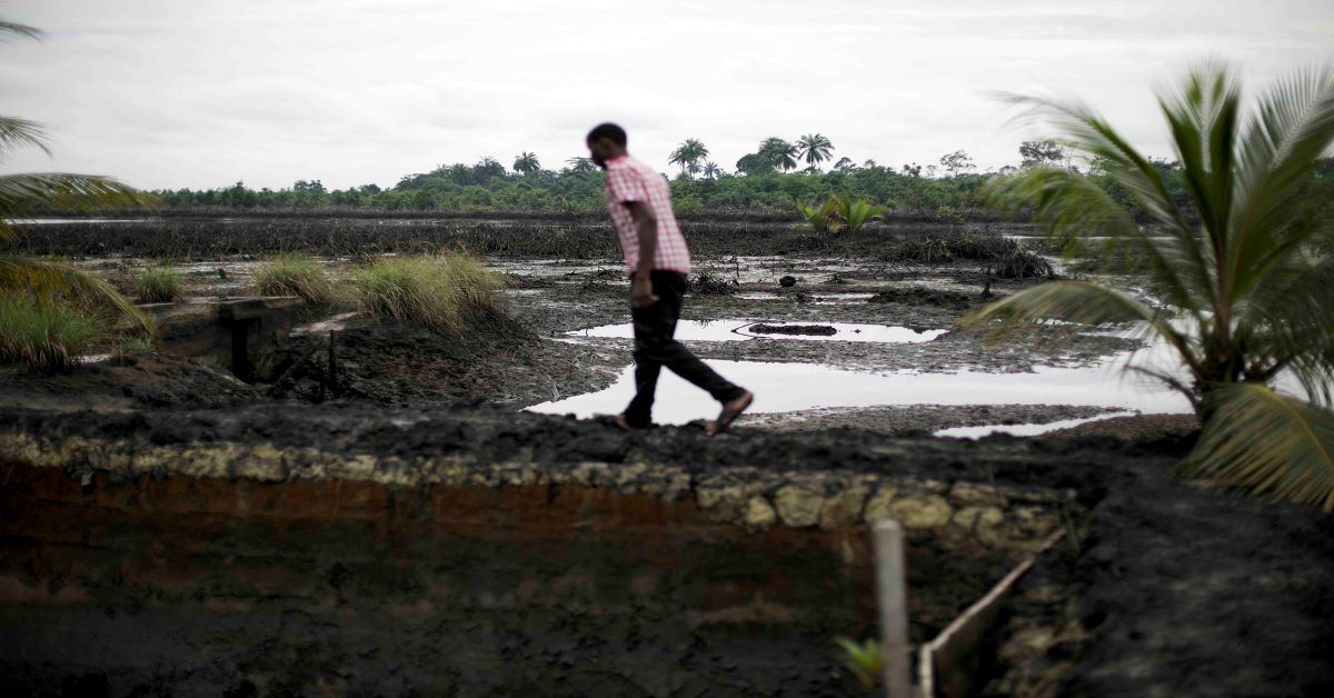 A man walks across a field polluted by oil