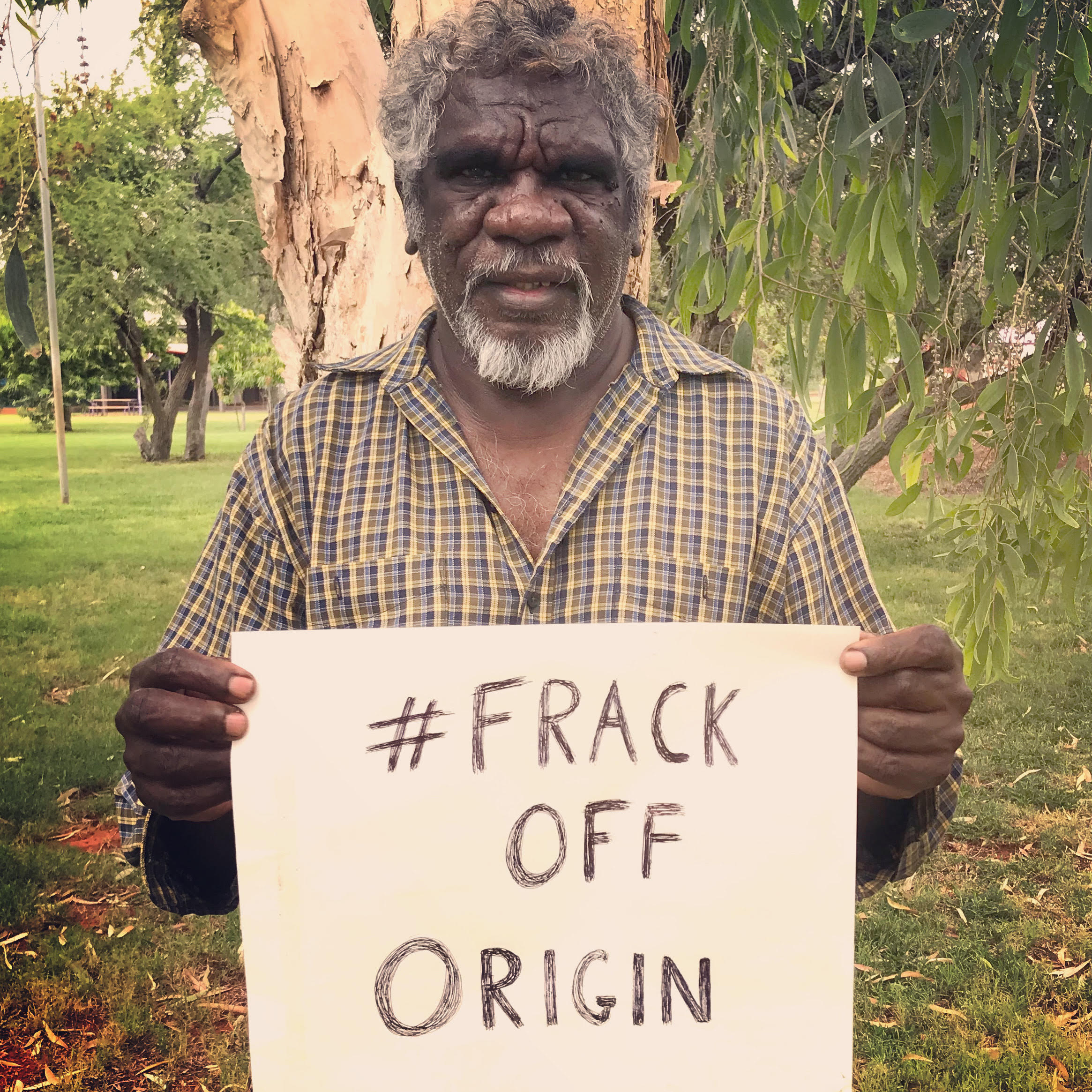 Mudburra Traditional Owner and Native Title Holder Ray Dimakarri Dixon from Marlinja NT holding a handwritten sign that says #frack off origin