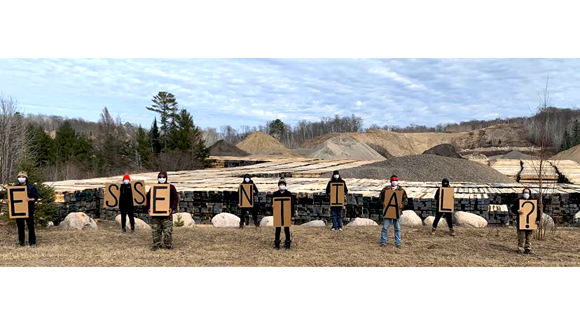 9 protesters/protectors at the Enbridge Line 3 tar sands pipeline construction maintaining physical distancing and holding placards spelling "E.S.S.E.N.T.I.A.L.?"