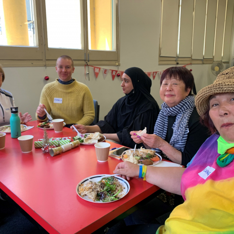 A group of colourfully dressed older and younger women sit together around a table.