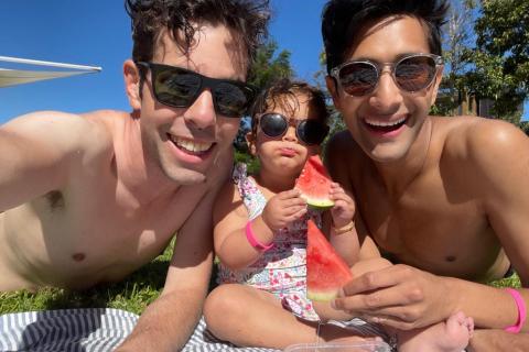 Adrian, Jasmine, and Govind are at the beach. They are smiling at the camera.