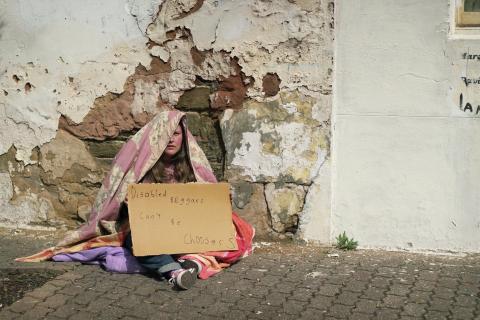 Kathryn Hall (Homeless person) with a blanket over head holding a sign saying Disabled beggars can't be choosy