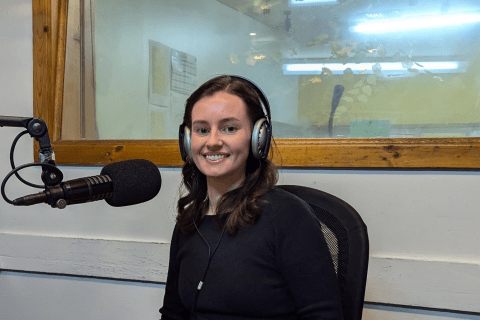 Betty Melon smiling in the 3CR Studio, sitting at the microphone with headphones on.