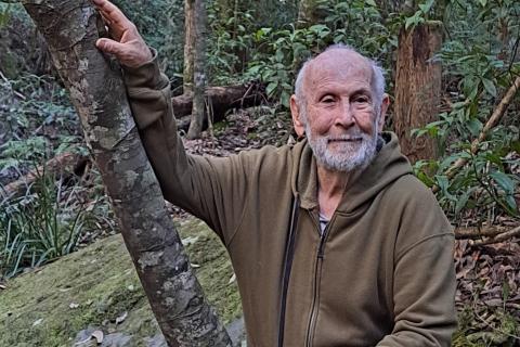 An older man with his hand on a tree trunk