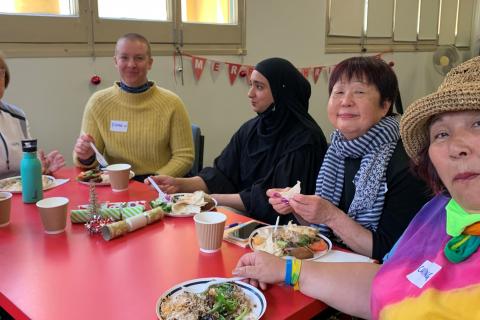 A group of colourfully dressed older and younger women sit together around a table.