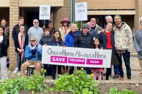 A group of residents standing outside a house with a banner reading Once A Home, Always A Home: Save Techno Park